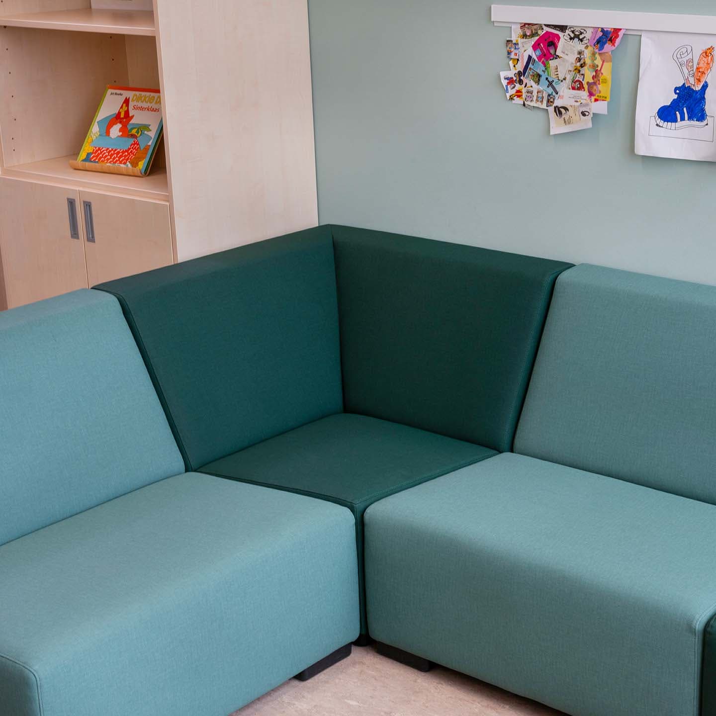 Zithoek met een turquoise hoekbank, kinderboeken binnen handbereik en kleurrijke tekeningen aan de muur.
