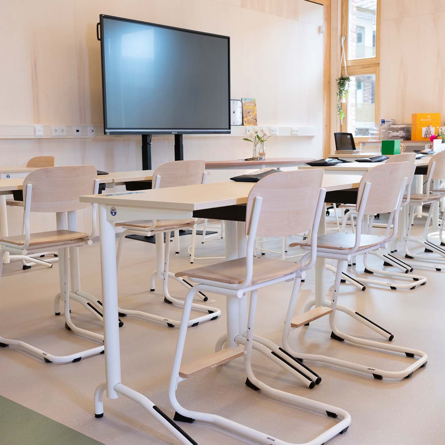 Modern klaslokaal met houten kinderstoelen, tafels en een groot digitaal scherm