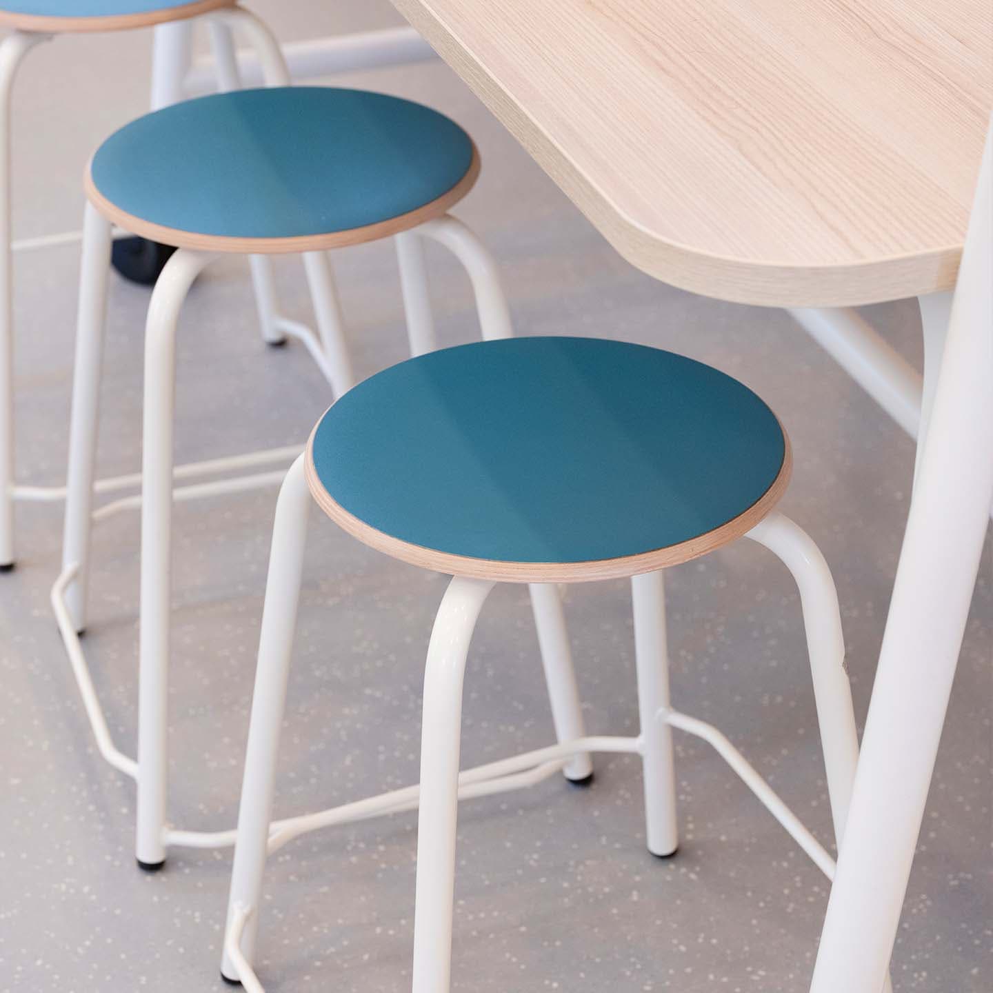 Drie krukken met blauwe zittingen en witte poten onder een lichthouten tafel.