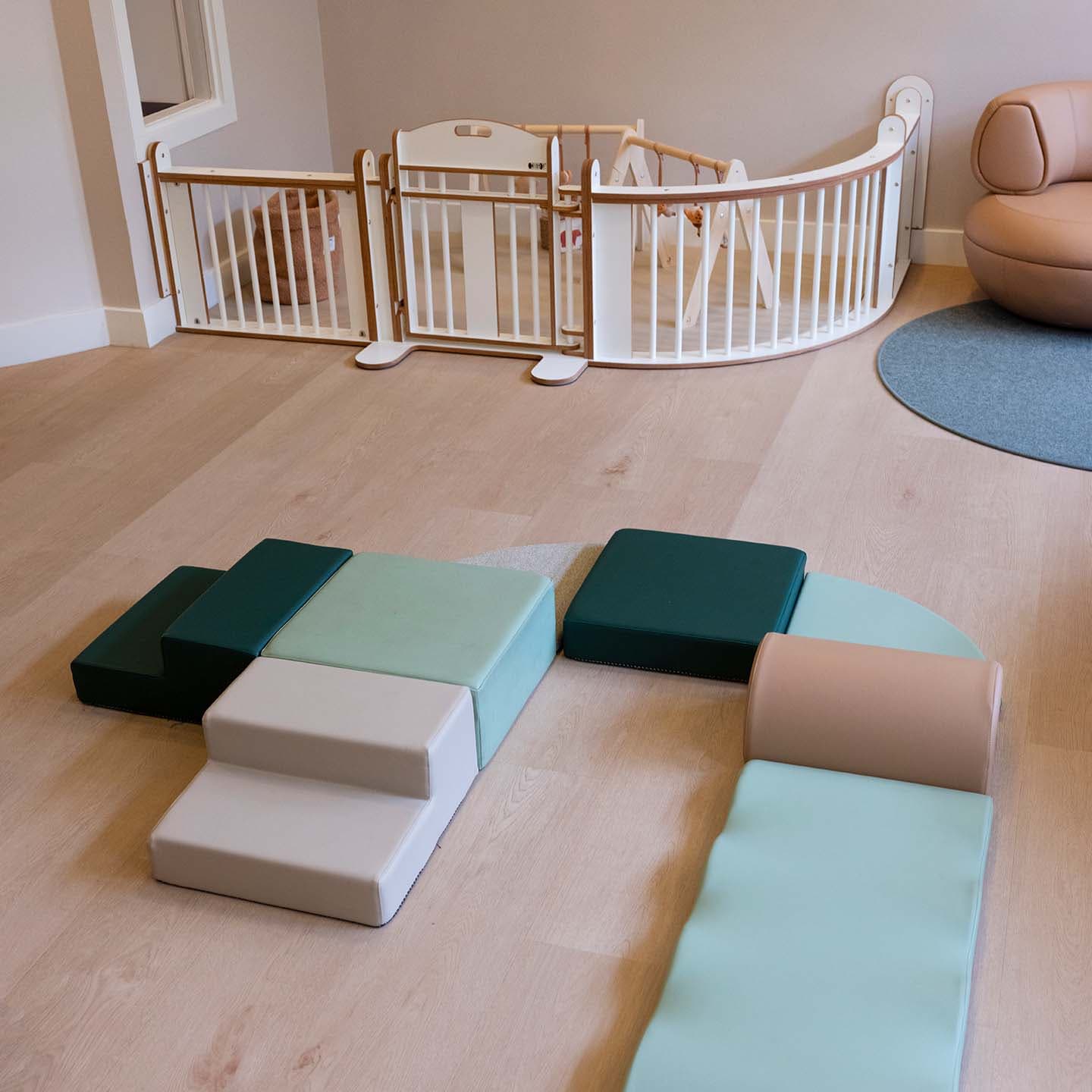 Speelruimte voor de babygroep op de kinderopvang waar een softplay kruipeiland in groen tinten op de grond ligt, en een houten grondbox op de achtergrond staat.