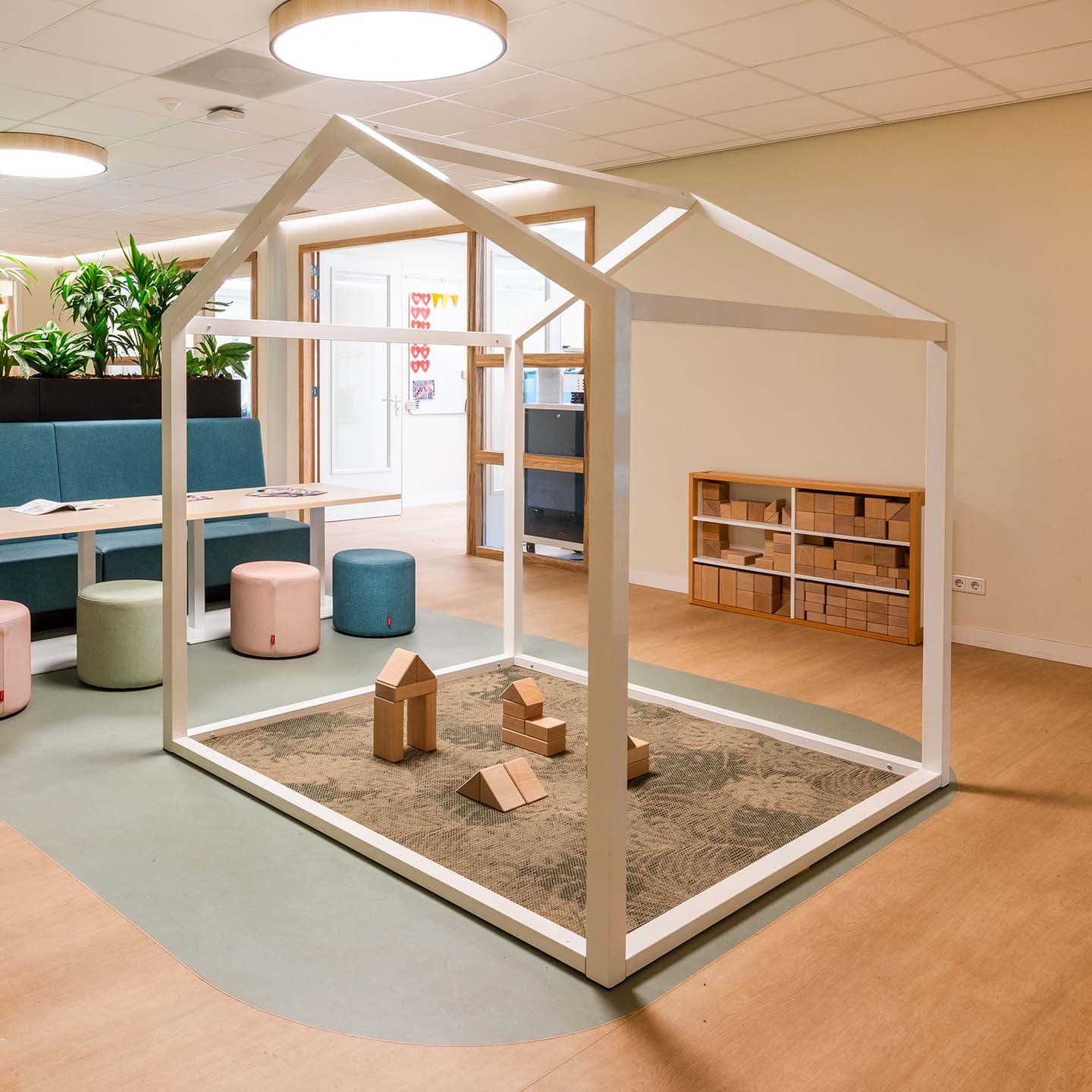Speelhuis van een stalen frame met daaronder een vloerkleed en houten blokken om mee te spelen.