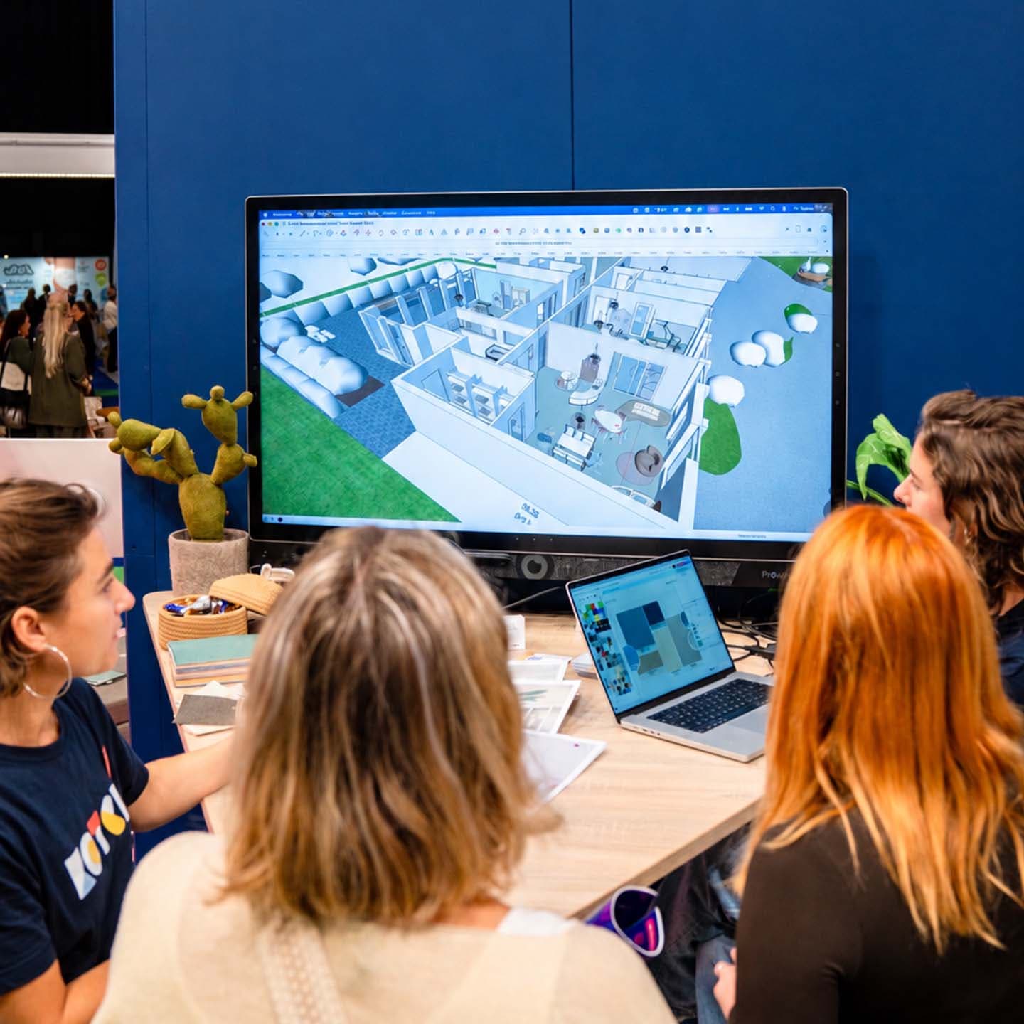 Vier mensen werken samen aan een bureau en bekijken een 3D-model van een gebouw op een groot scherm, met een laptop waarop ontwerpopties worden getoond.