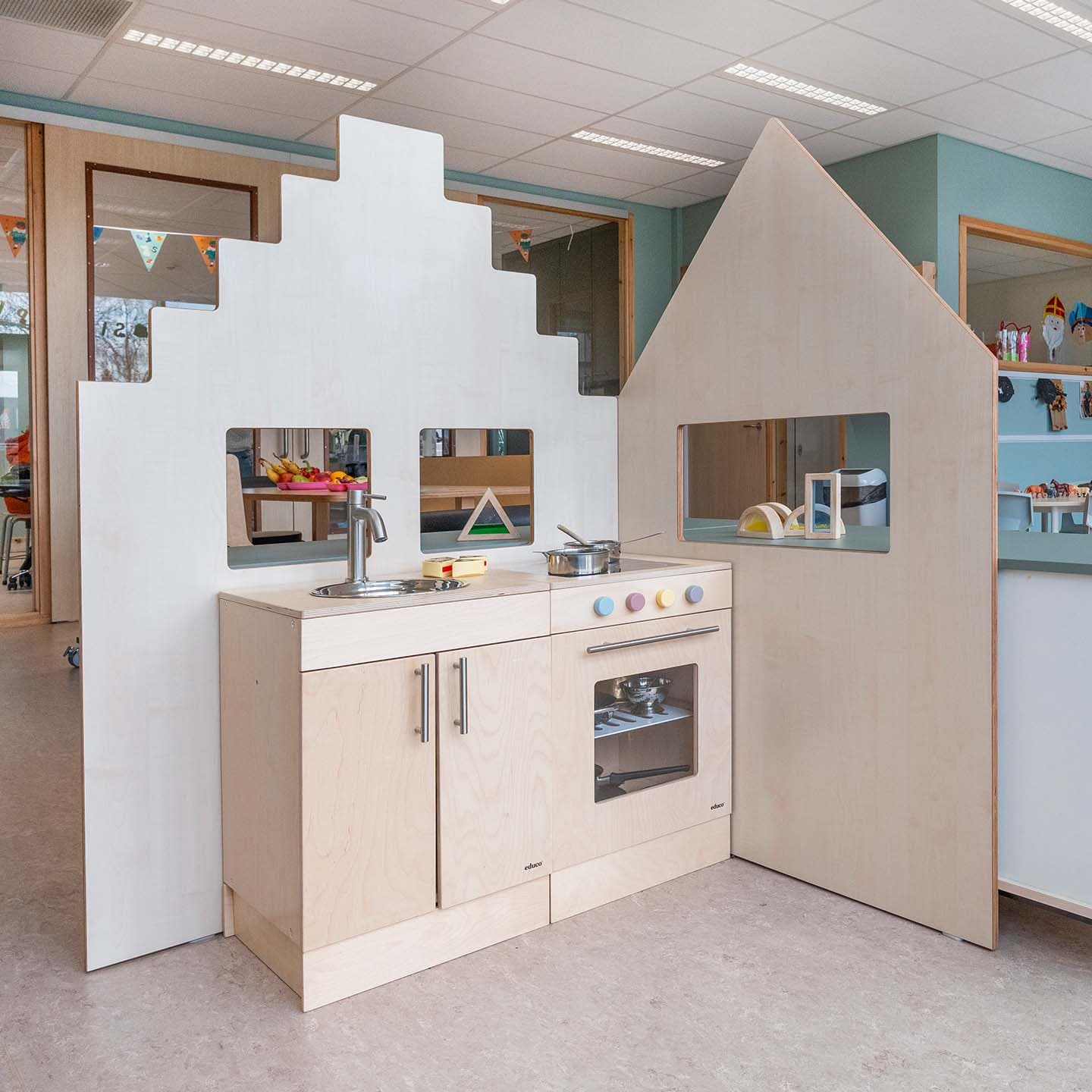 Houten kinderkeuken met fornuis, spoelbak, oven en pannen, omring door een huisvormige speelconstructie.