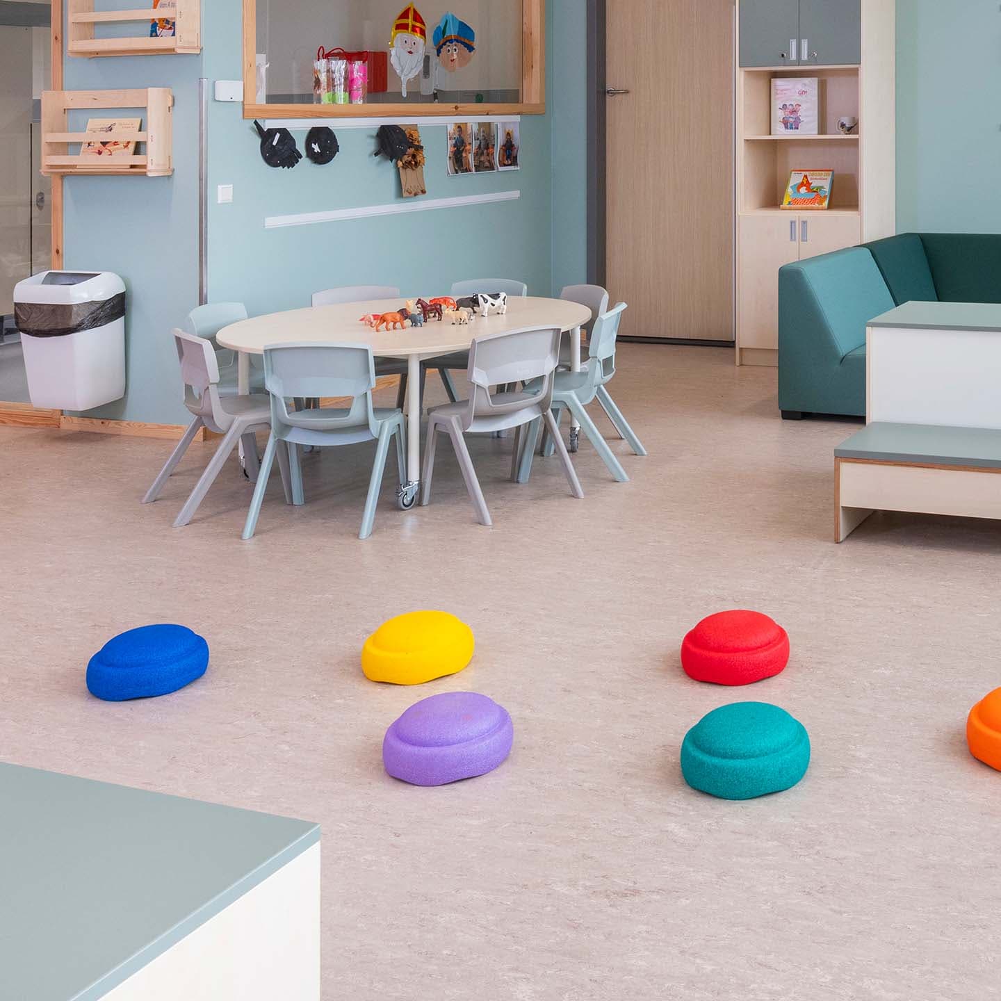 Open groepsruimte in de kinderopvang waar op de vloer gekleurde stapelstenen zijn uitgelegd om over heen te lopen.