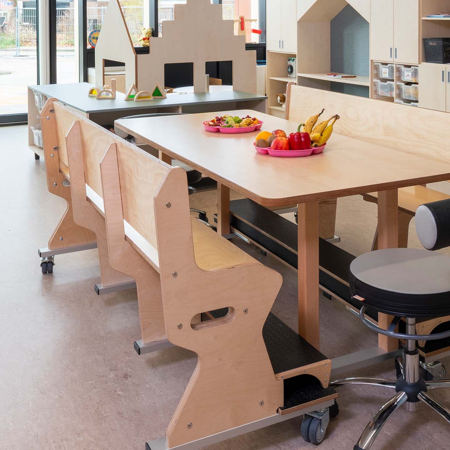 Groepsruimte in de kinderopvang met een eettafel, ergonomische verrijdbare houten banken en een leidsterstoel.