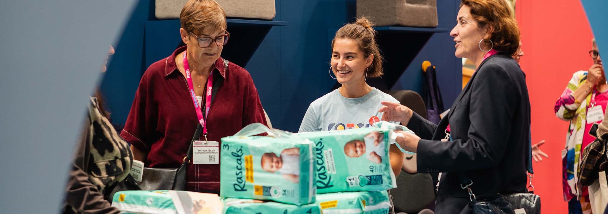 Twee vrouwen praten aan een tafel met pakken Rascals-luiers in beeld; een van hen draagt een naamkaartje.