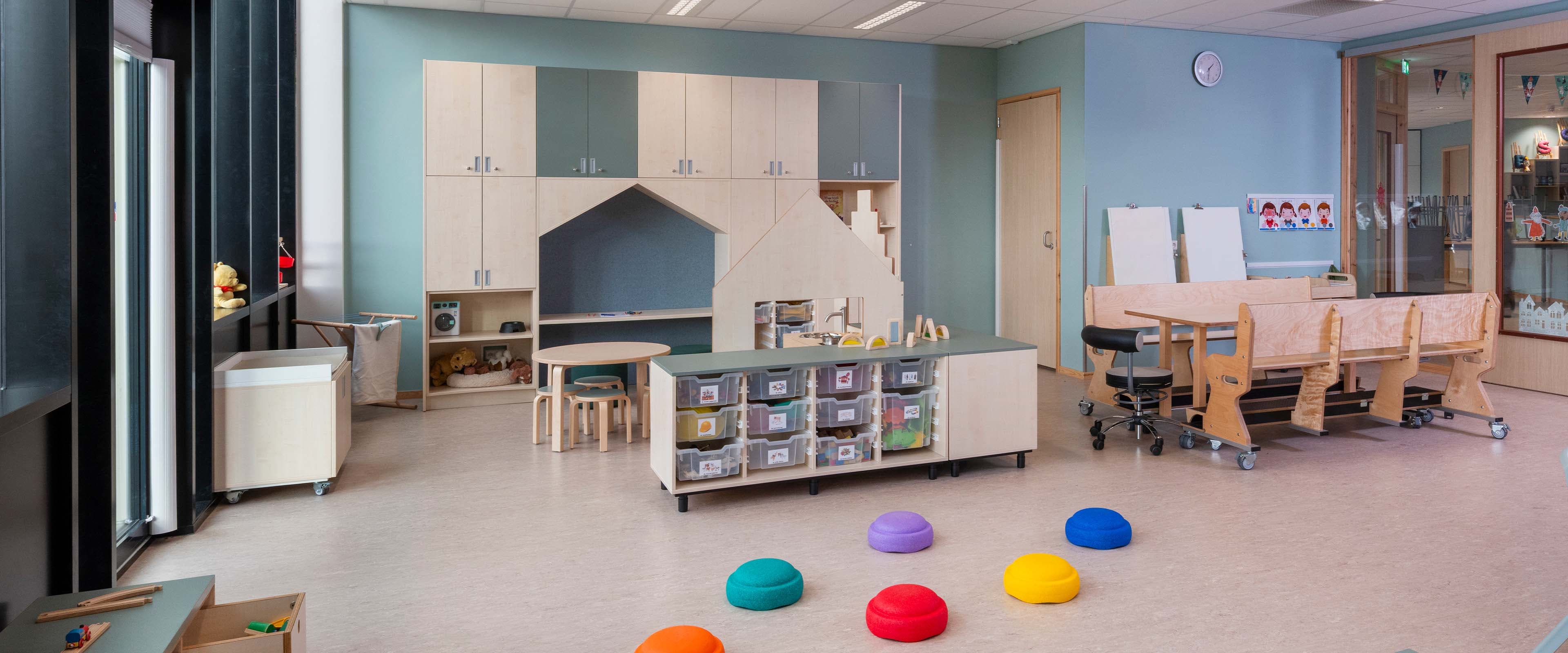 Groepsruimte in de kinderopvang met verrijdbaar meubilair, waaronder een houten tafel, houten banken, lage opbergkasten en een op maat gemaakte houten kast.